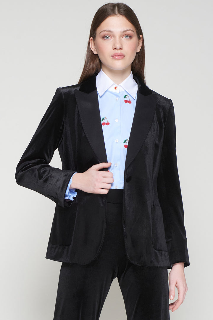 Person wearing a black suit with a light blue shirt featuring red cherries on a plain background