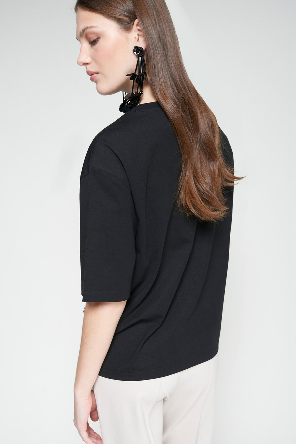 Woman wearing a black top and white pants against a plain background