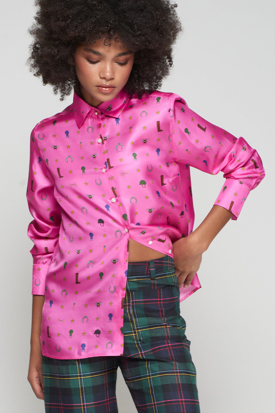 Person wearing a pink satin shirt with colorful patterns and plaid pants on a plain background