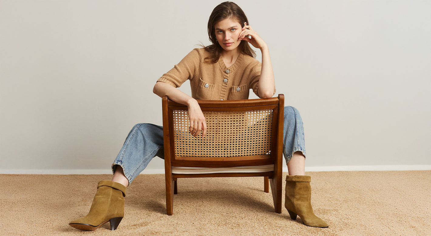 Woman sitting on a wooden chair with a woven backrest, wearing a brown top and blue jeans.