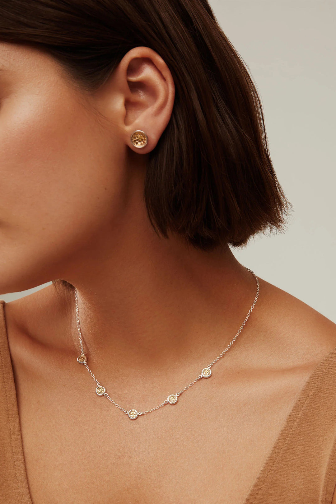 Close-up of a person wearing gold earrings and a delicate necklace against a neutral background