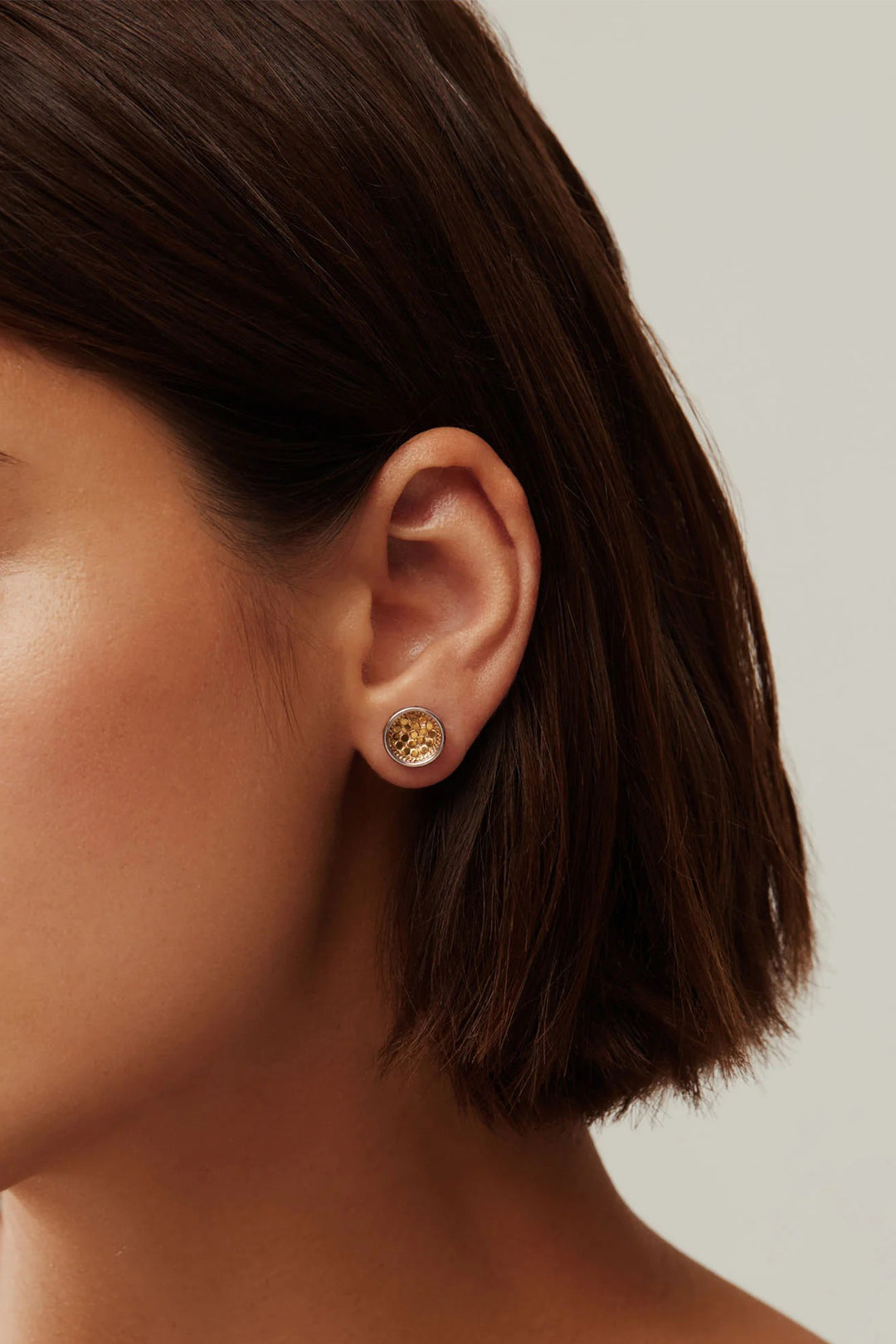 Close-up of an ear wearing a gold earring with a neutral background