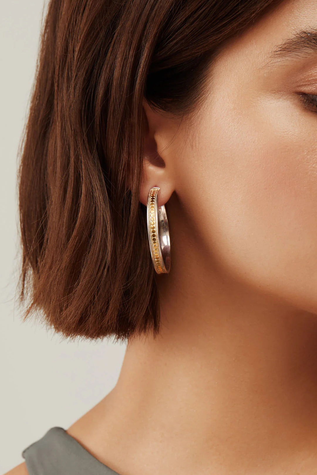 Close-up of a person wearing gold hoop earrings with a neutral background