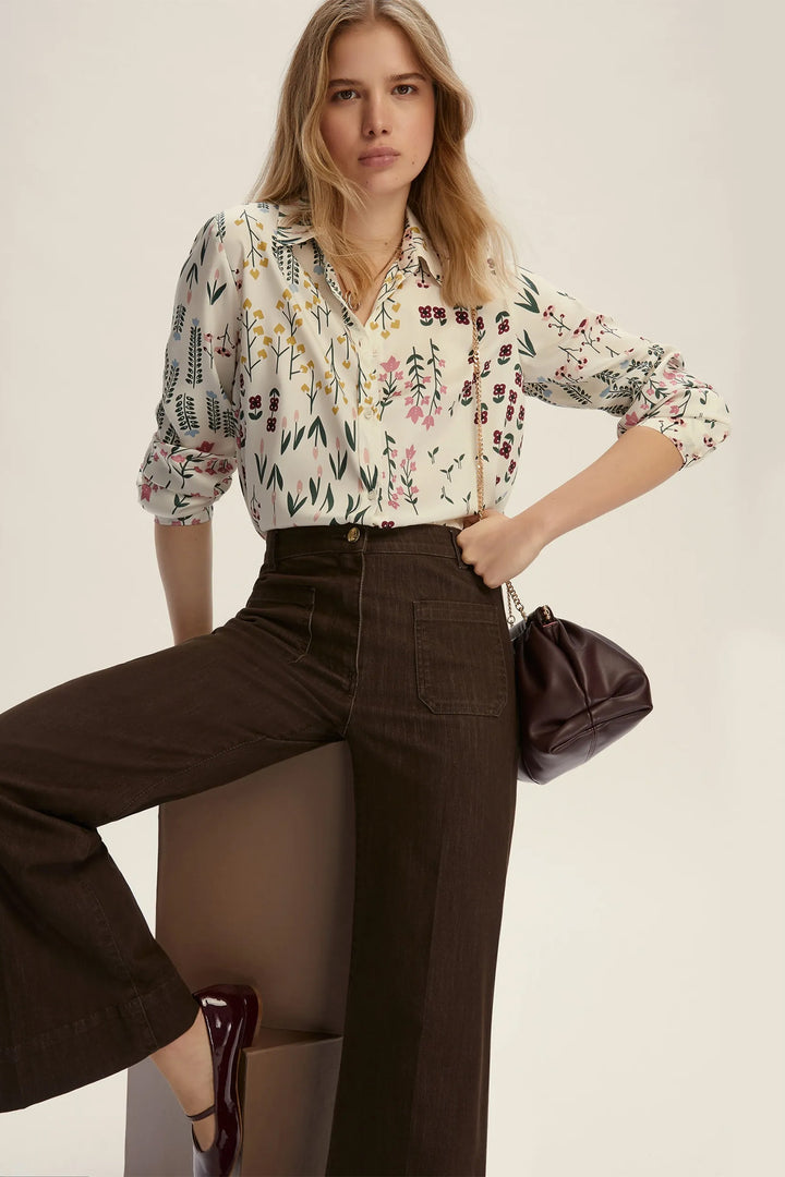 Woman wearing a floral blouse and brown pants with a neutral background