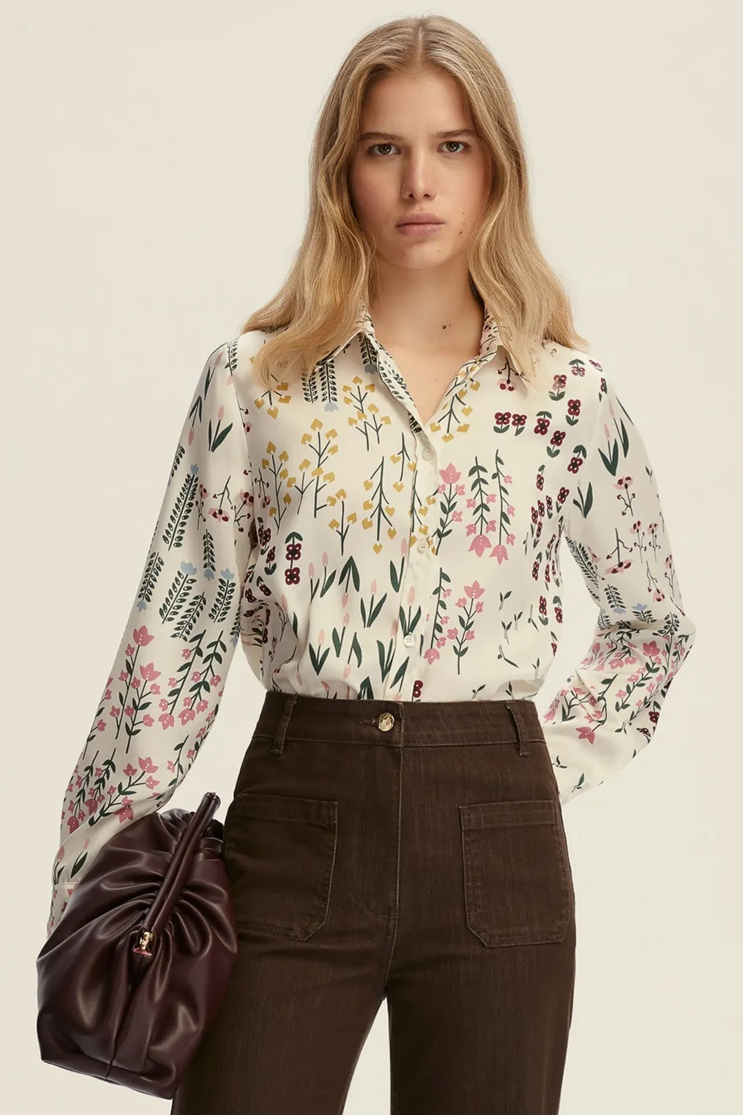 Woman wearing a floral blouse and brown pants with a beige background