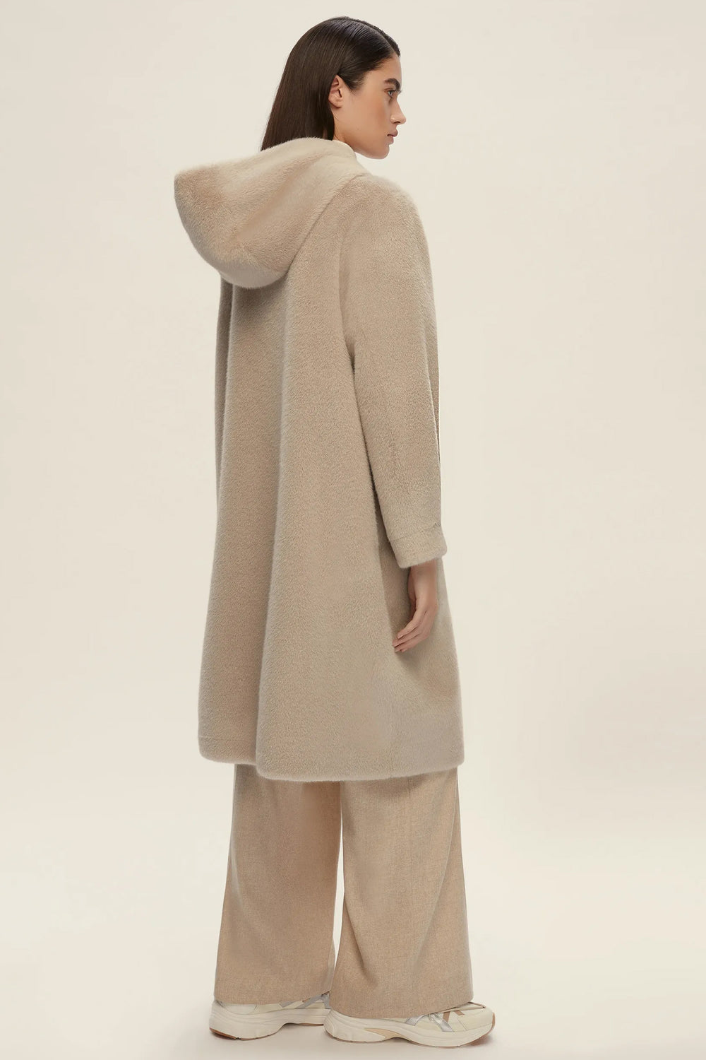 Person wearing a beige hooded coat and pants on a plain background