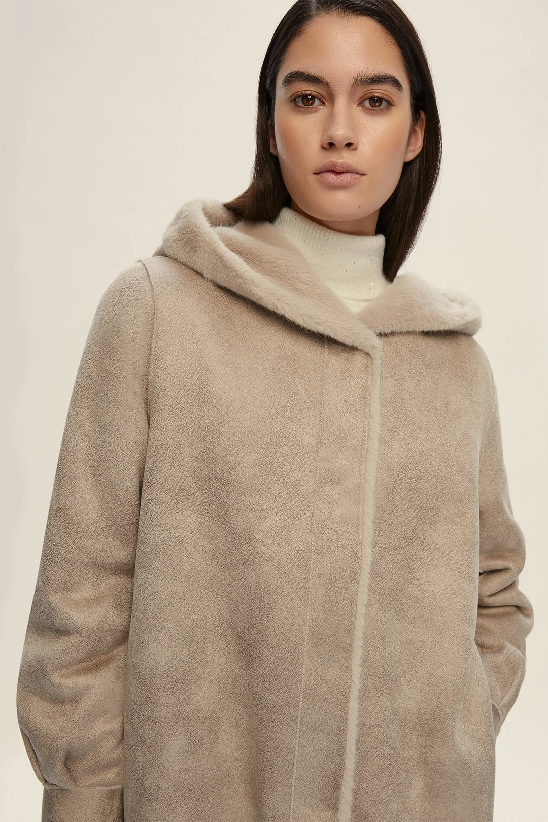 Woman wearing a beige coat with a fur-lined hood on a plain background