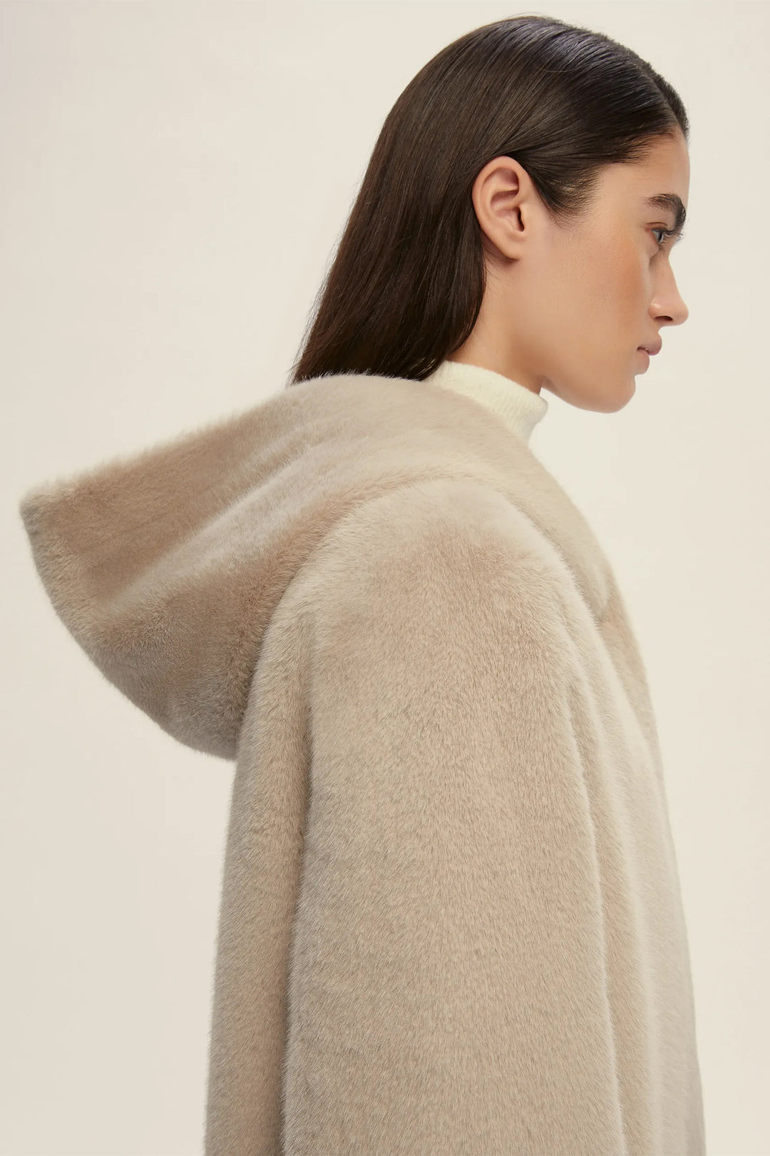Woman wearing a beige hooded coat against a plain background