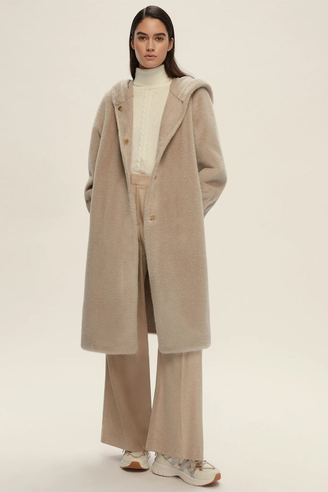 Woman wearing a beige coat, turtleneck, and wide-leg pants on a plain background