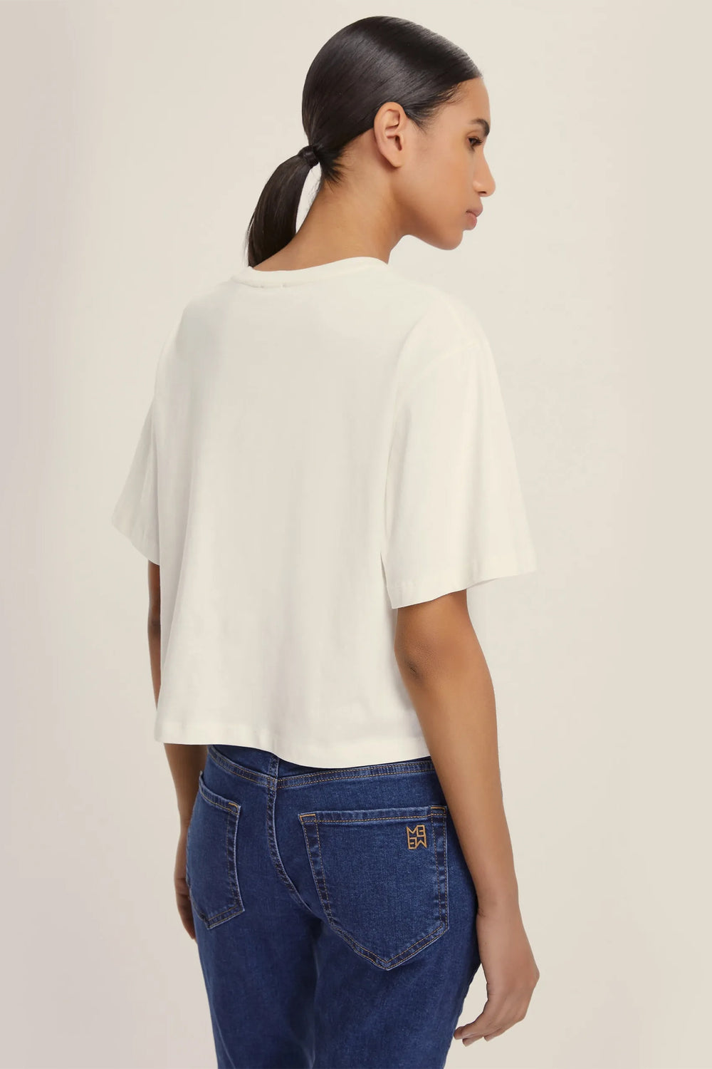 Woman wearing a white top and blue jeans on a plain background