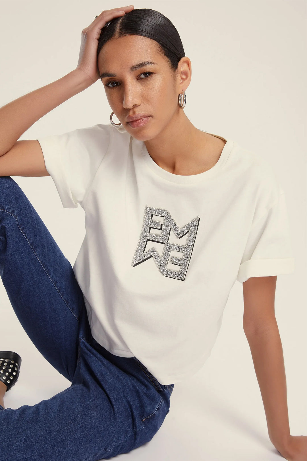 Woman wearing a white t-shirt with a logo and blue jeans on a plain background