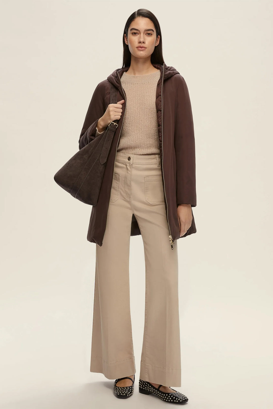 Woman wearing a brown coat over a beige sweater and pants on a plain background
