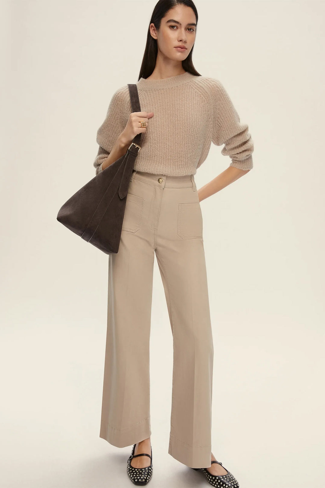 Woman wearing a beige sweater and pants with a brown bag on a light background