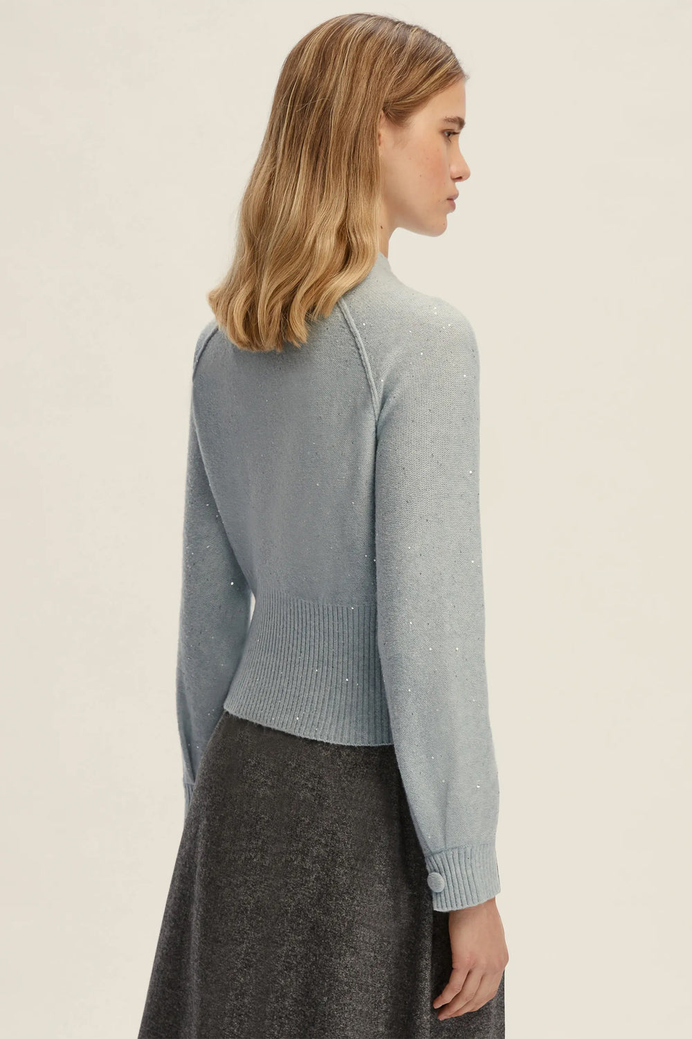 Woman wearing a light gray sweater and dark gray skirt on a beige background
