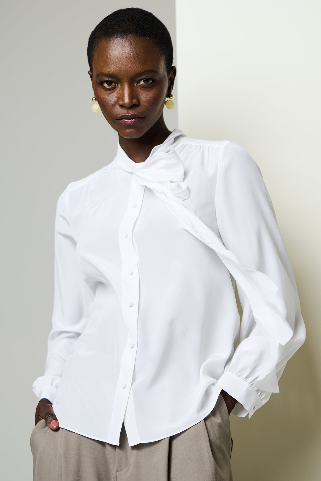 Woman wearing a white blouse with a bow detail against a plain background