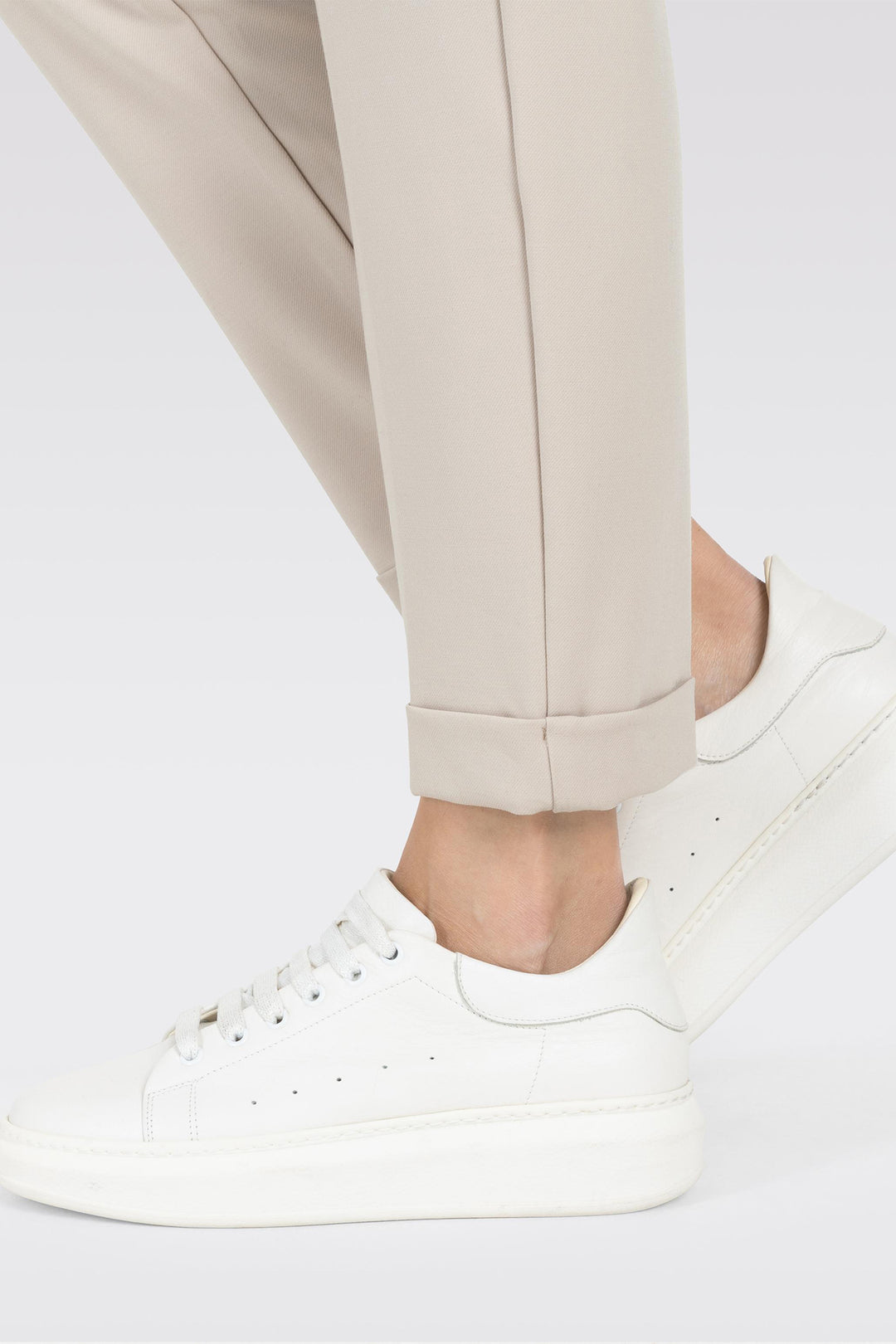 White sneakers worn with beige pants on a light gray background
