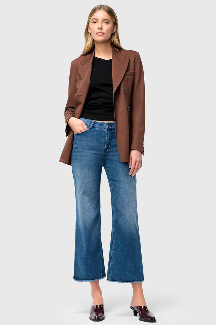 Woman wearing a brown blazer, black top, and blue jeans on a white background