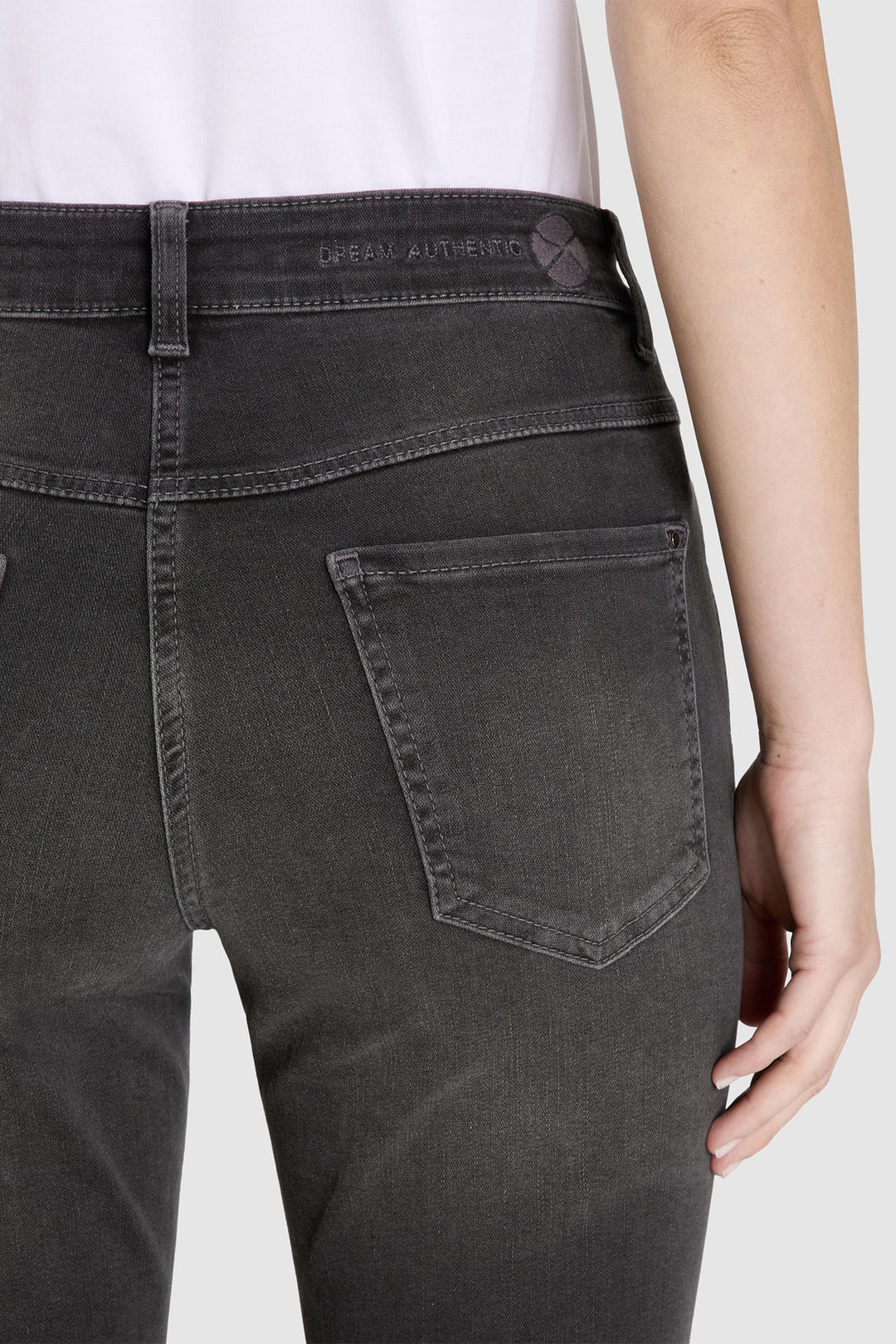 Close-up of a person wearing black jeans with a visible brand label on a white background