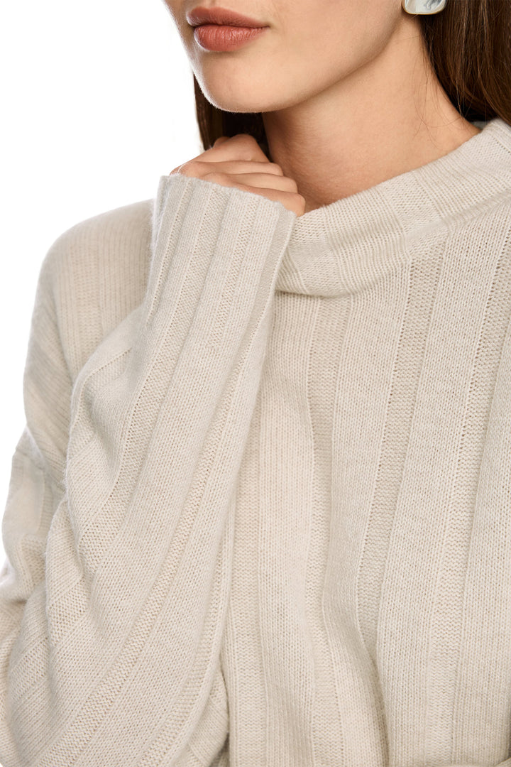 Close-up of a person wearing a beige ribbed sweater with a blurred background
