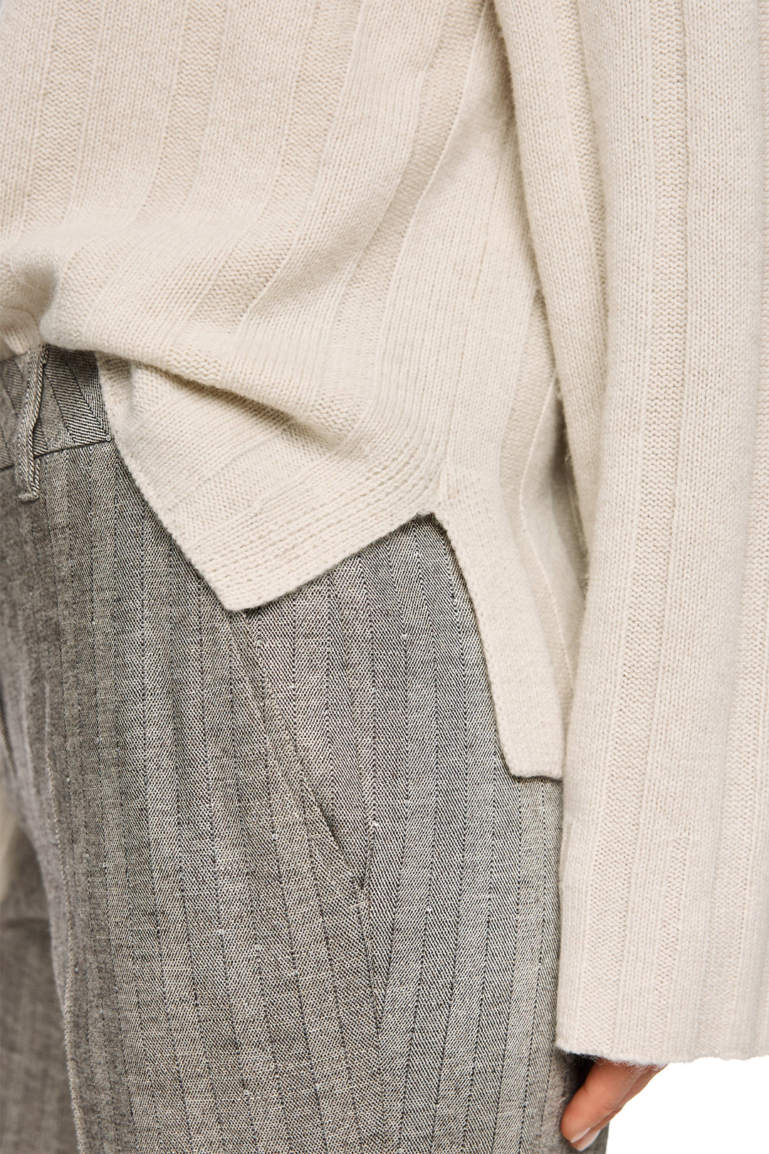 Close-up of a person wearing a beige sweater and gray pants.