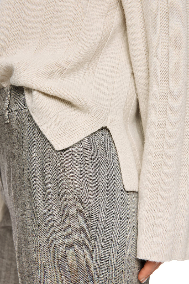 Close-up of a person wearing a beige sweater and gray pants.
