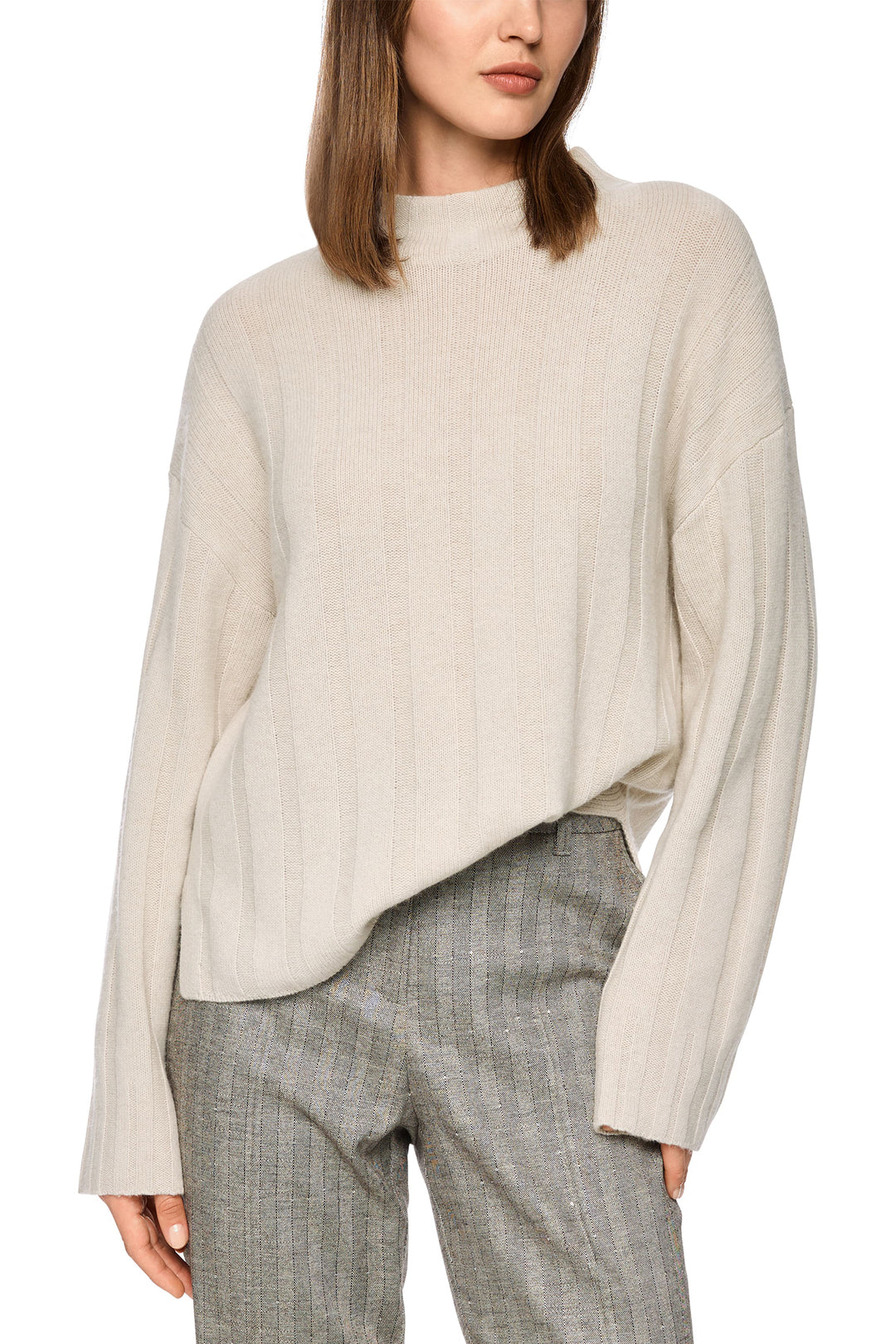 Woman wearing a beige sweater and gray plaid pants on a white background
