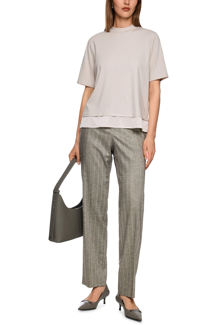 Woman wearing a beige top and gray checkered pants, holding a gray handbag on a white background