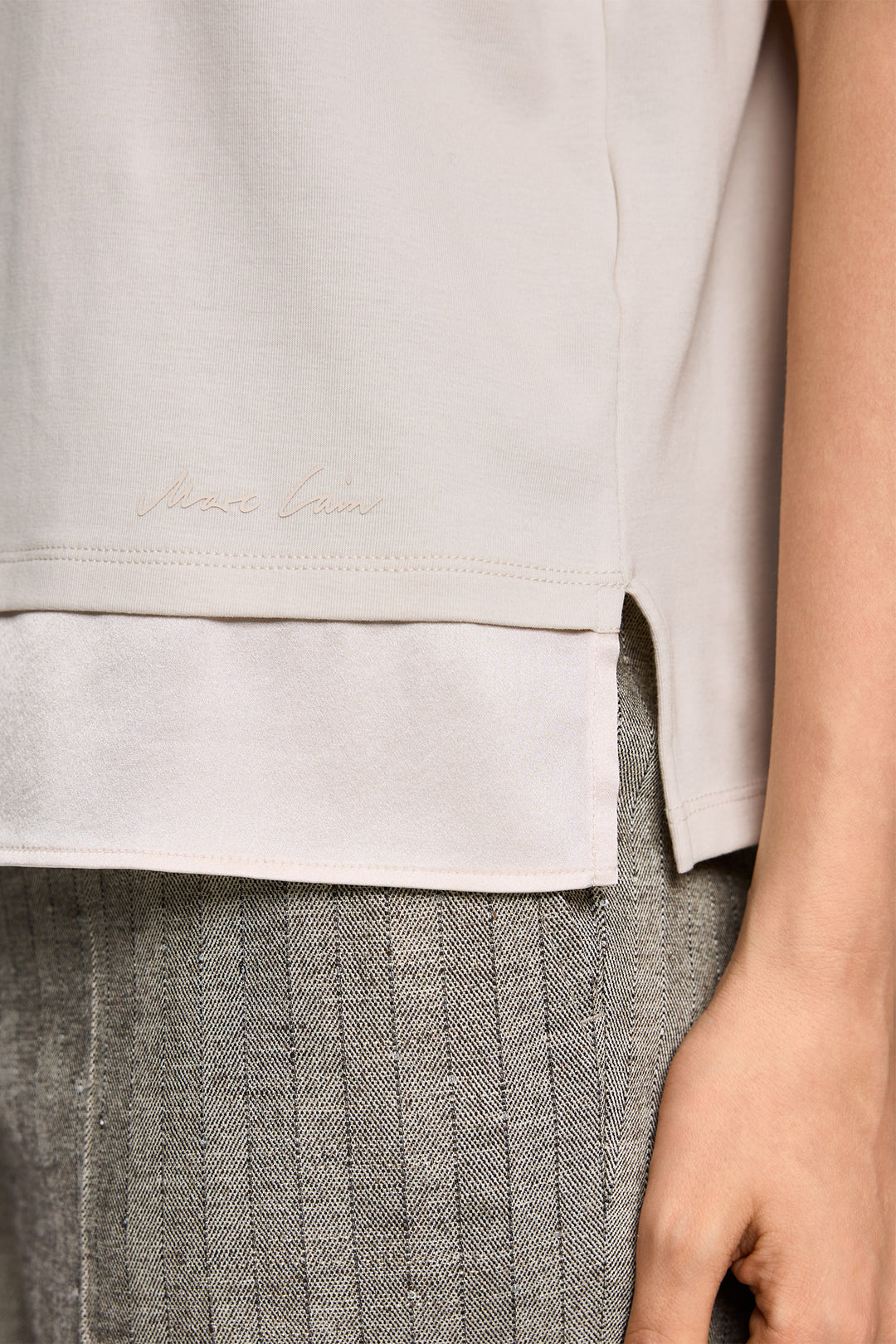Close-up of a person wearing a light gray shirt and gray pants with a visible brand logo.