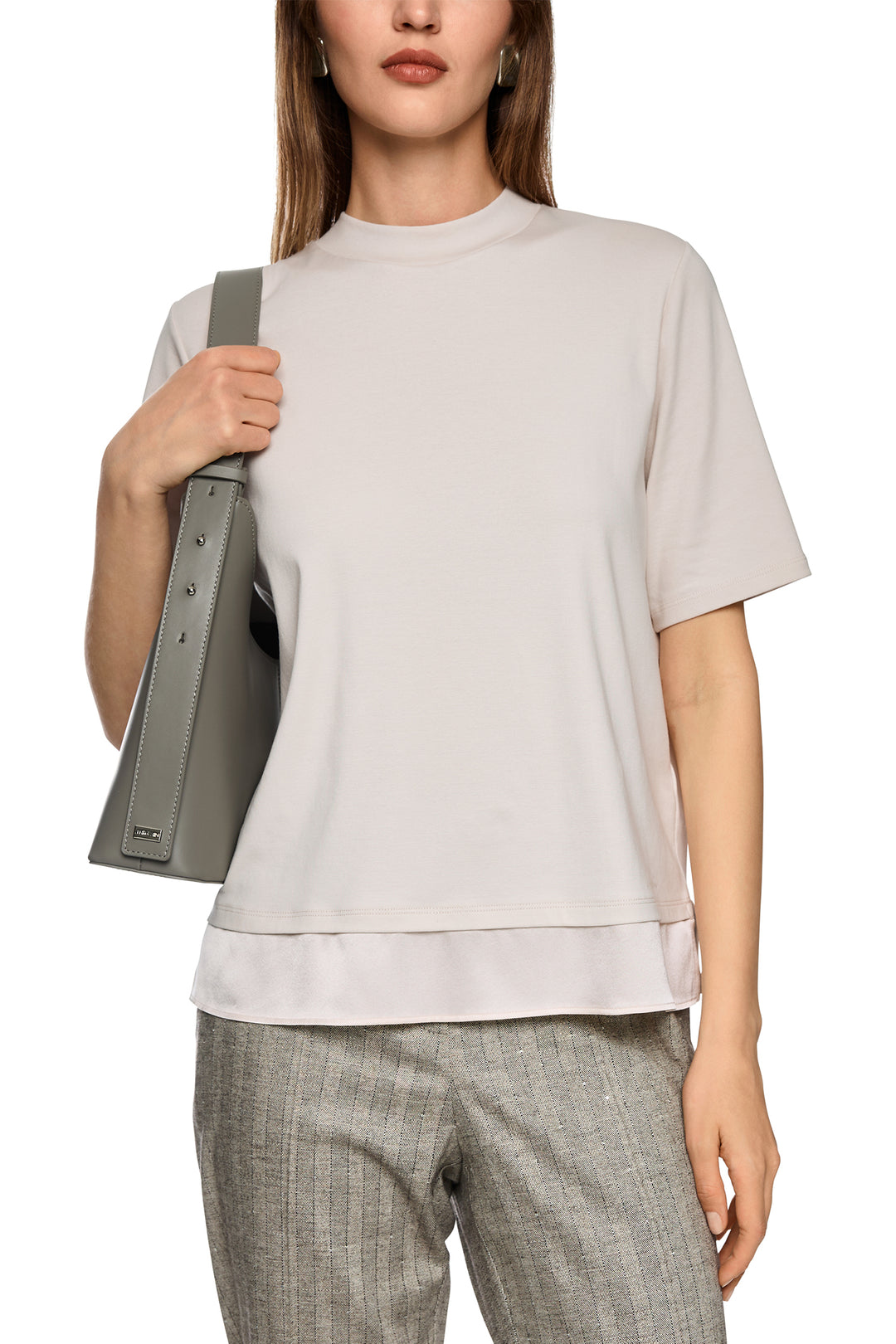 Woman wearing a light gray t-shirt and plaid pants, holding a gray bag.