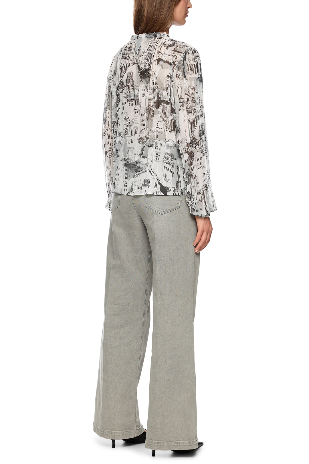 Woman wearing a patterned blouse and light gray pants on a white background