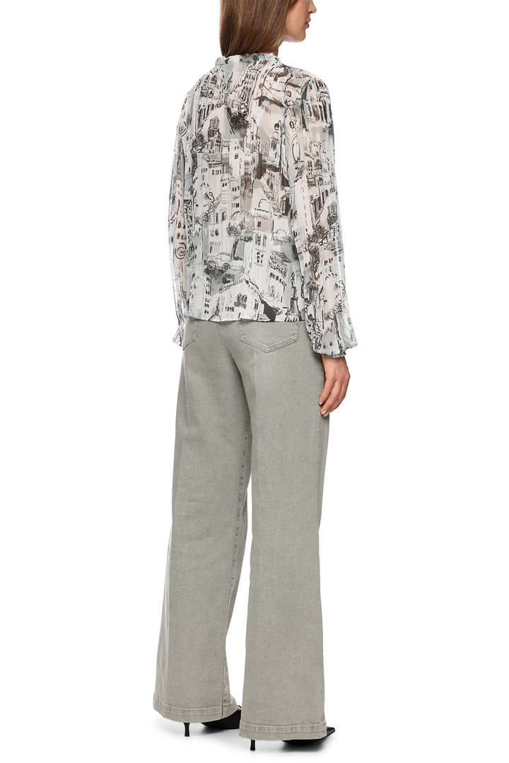 Woman wearing a patterned blouse and light gray pants on a white background