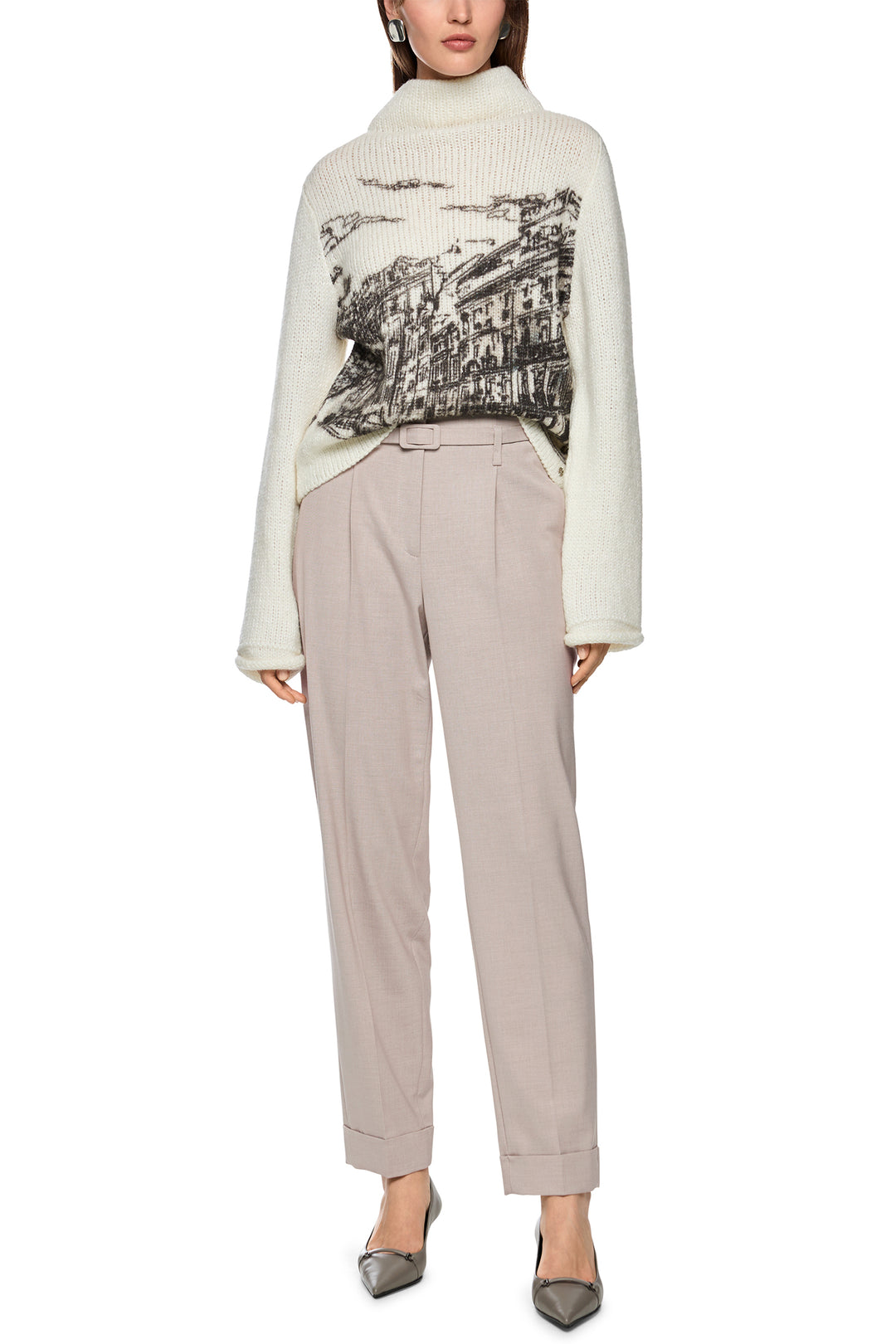 Woman wearing a white sweater with a graphic design and beige pants on a white background