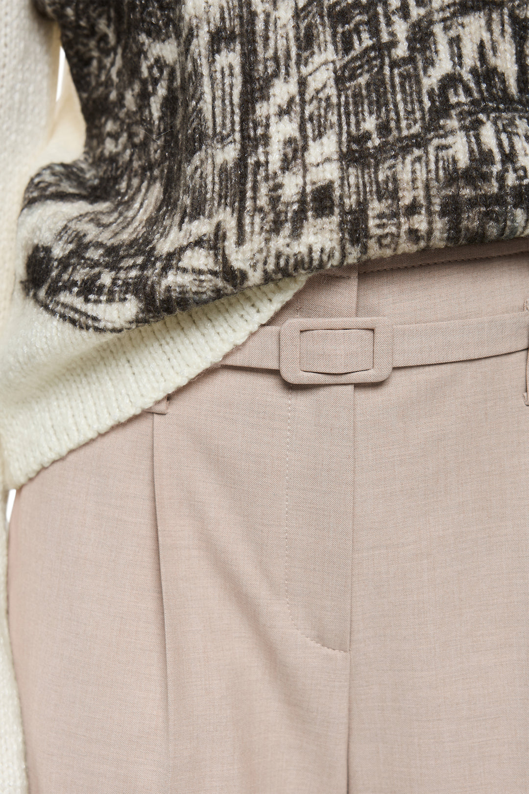 Close-up of a patterned sweater and beige pants with a belt.