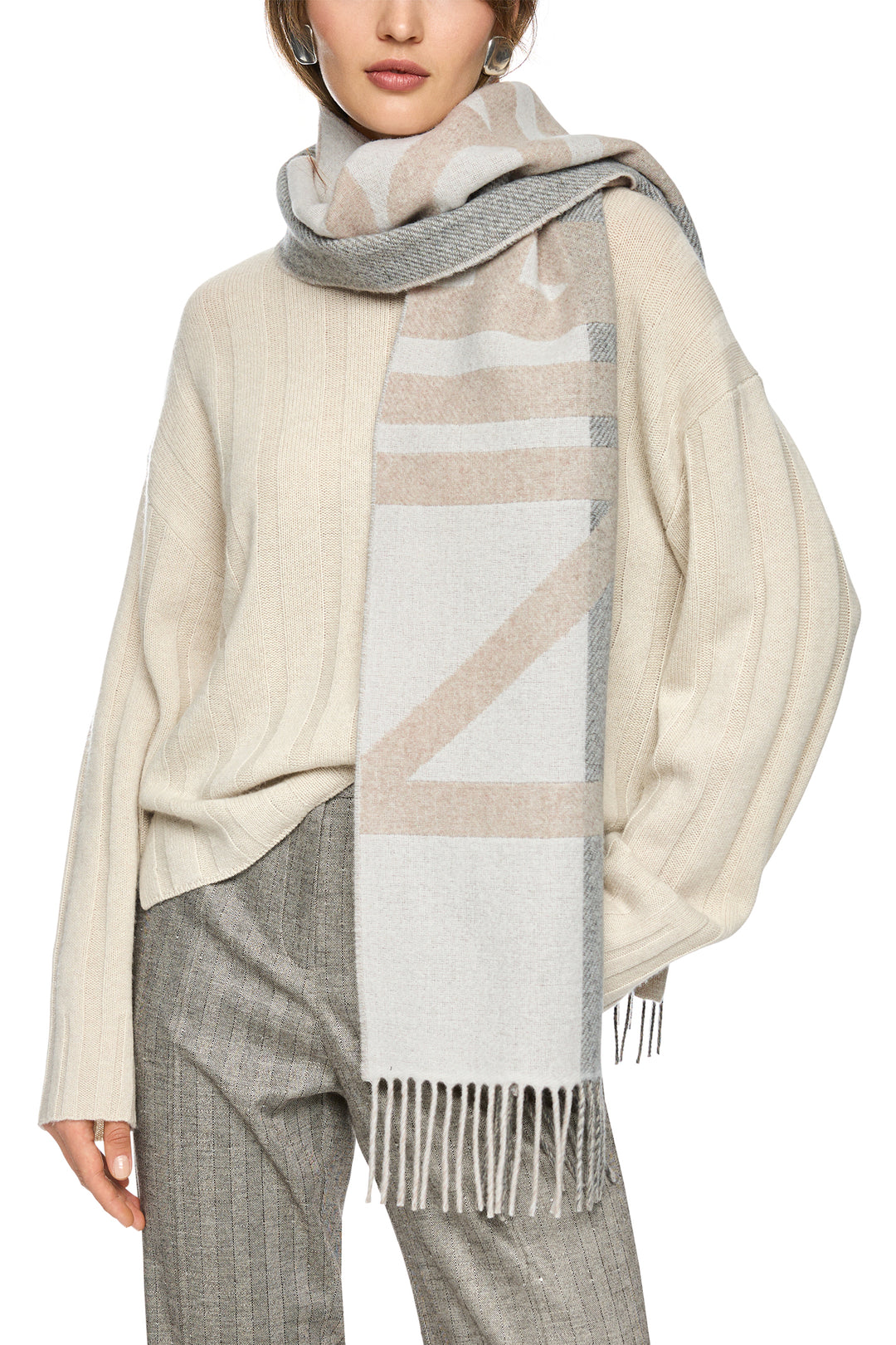 Person wearing a beige scarf with geometric pattern and fringe, over a neutral outfit.