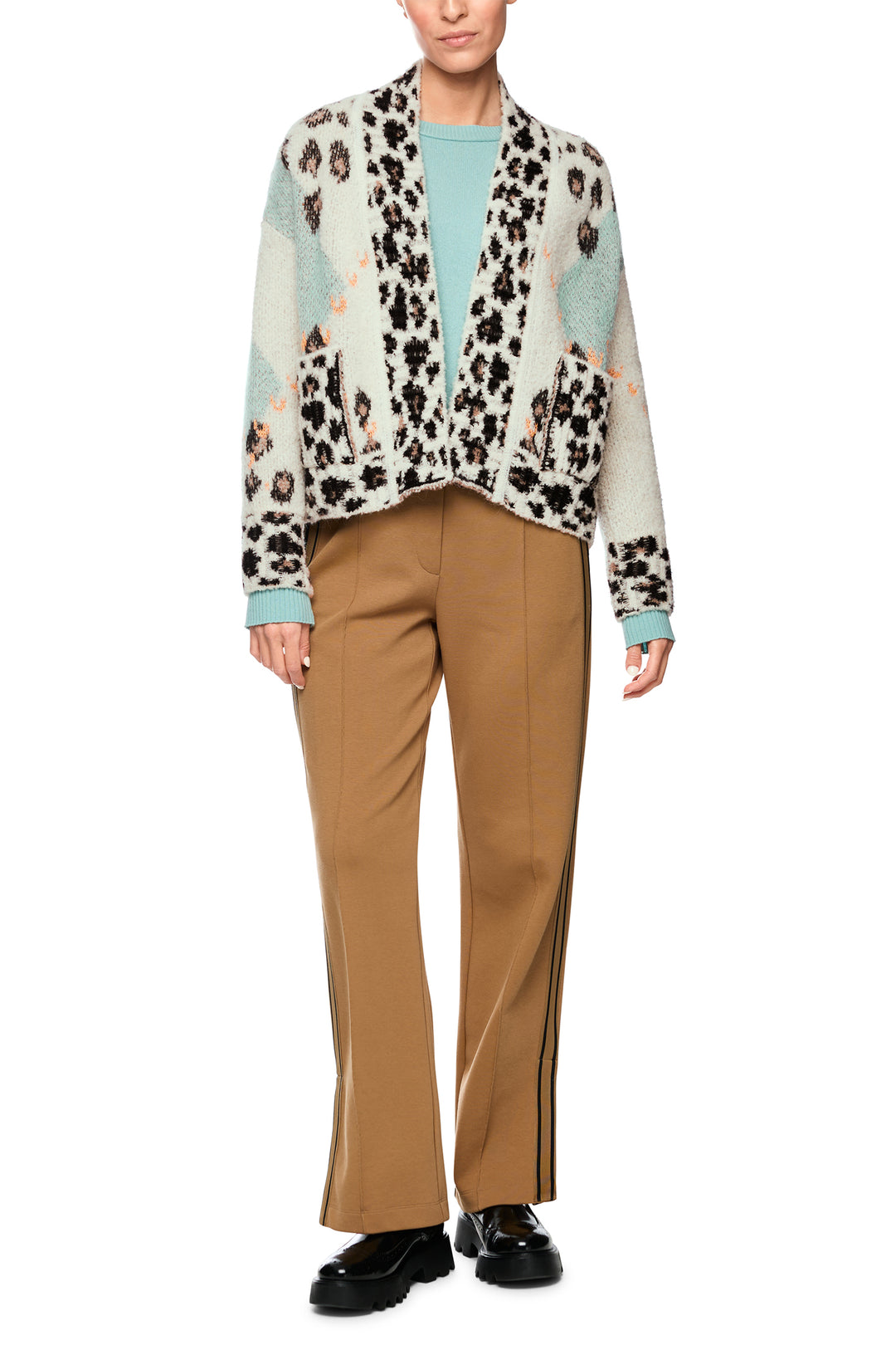 Person wearing a patterned shirt with a leopard print design, beige pants, and black shoes on a white background.