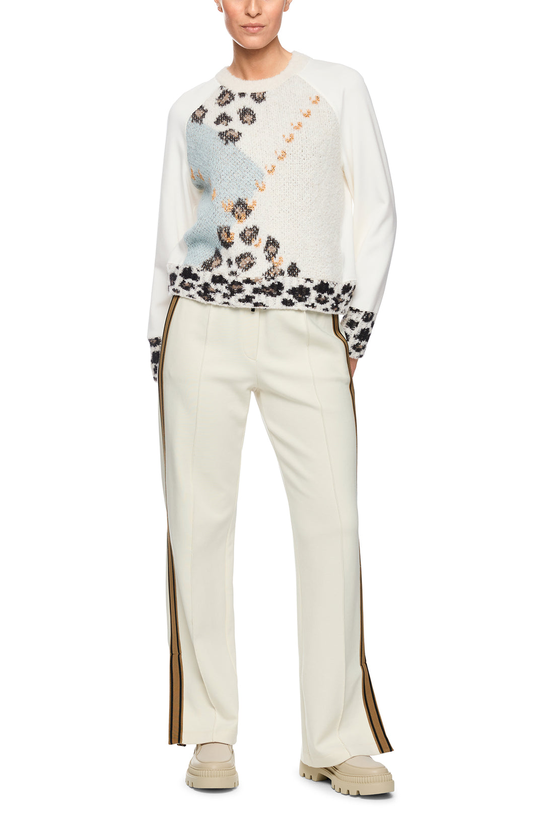 Person wearing a white sweater with floral patterns and beige pants on a white background