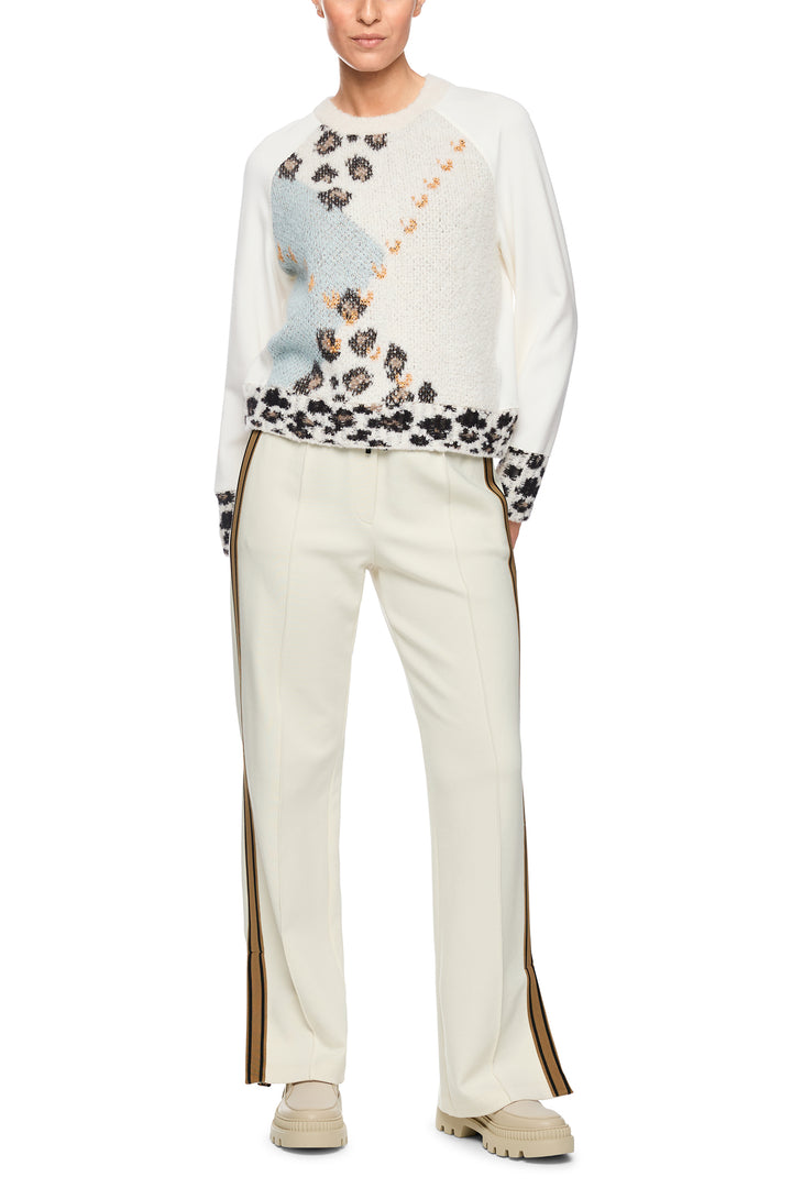 Person wearing a white sweater with floral patterns and beige pants on a white background