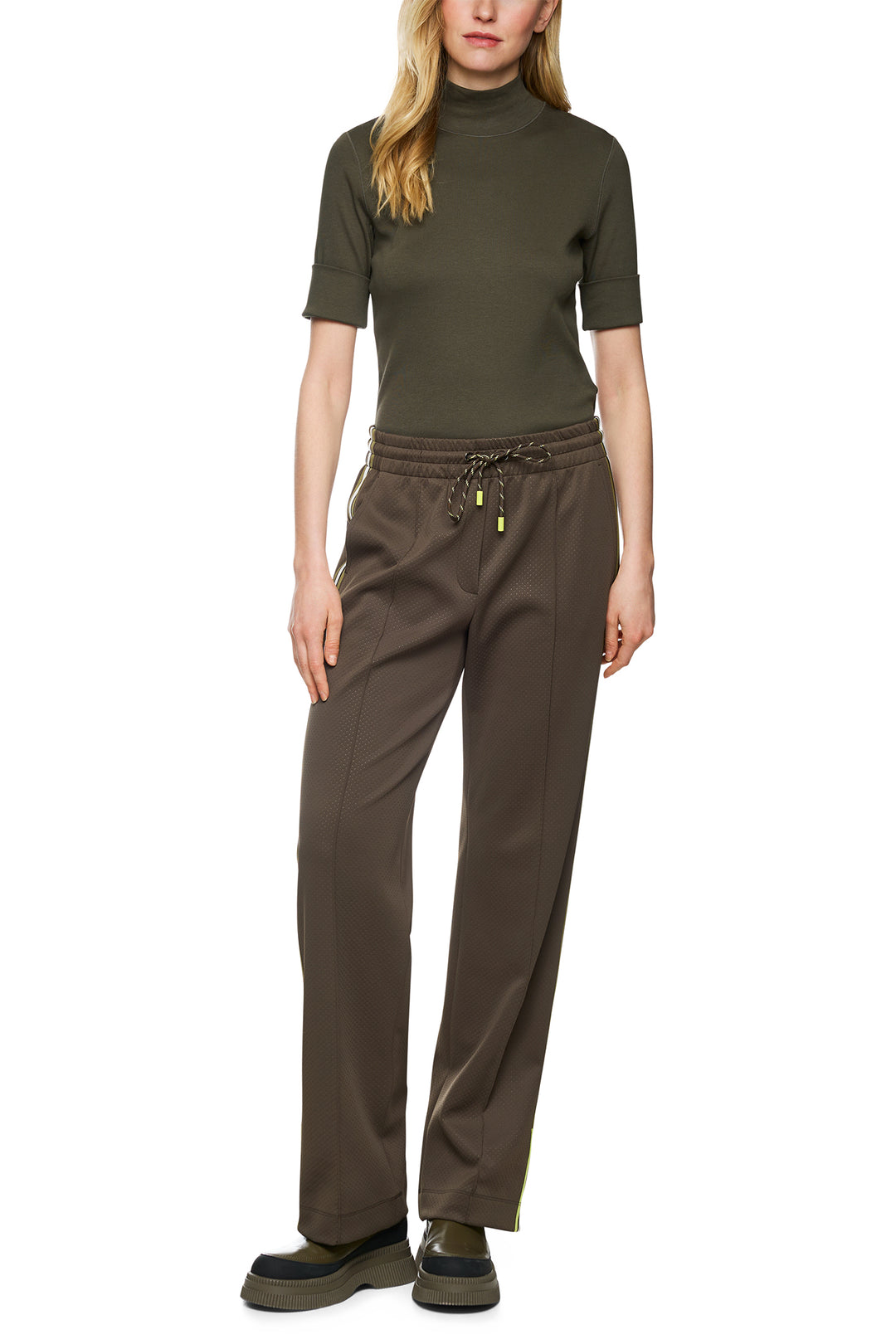 Woman wearing a green turtleneck and brown pants on a white background
