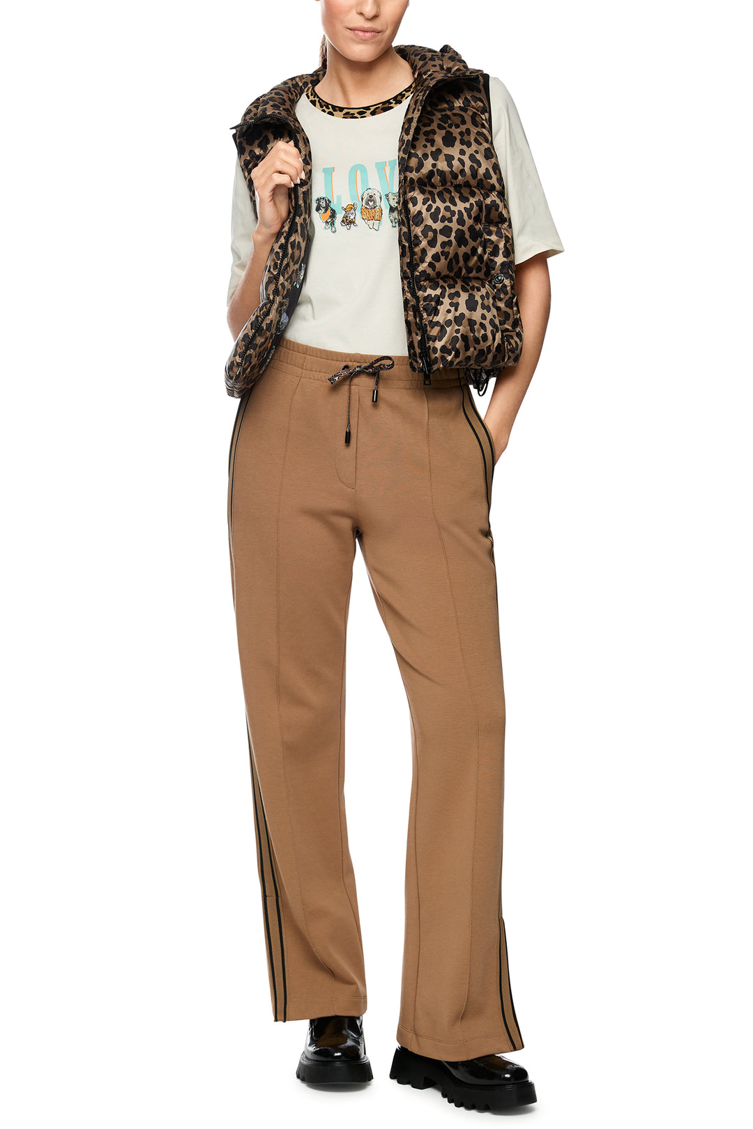 Person wearing a leopard print vest, white shirt with text, and brown pants on a white background