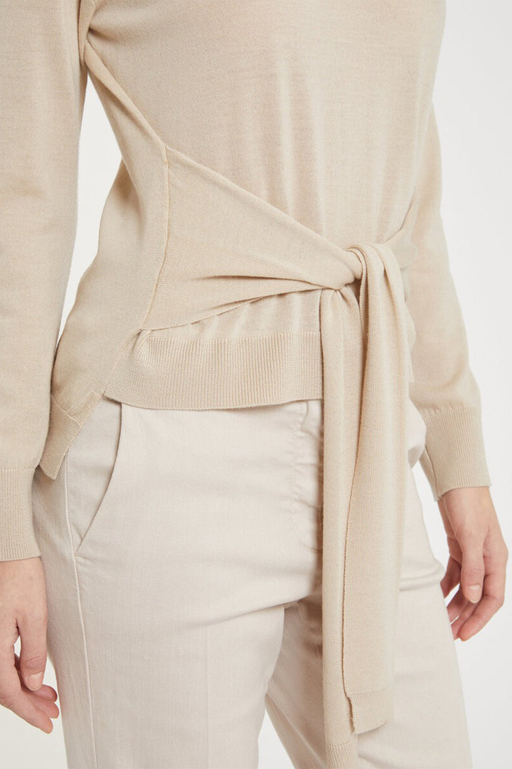 Beige sweater with a tie detail worn by a person on a white background