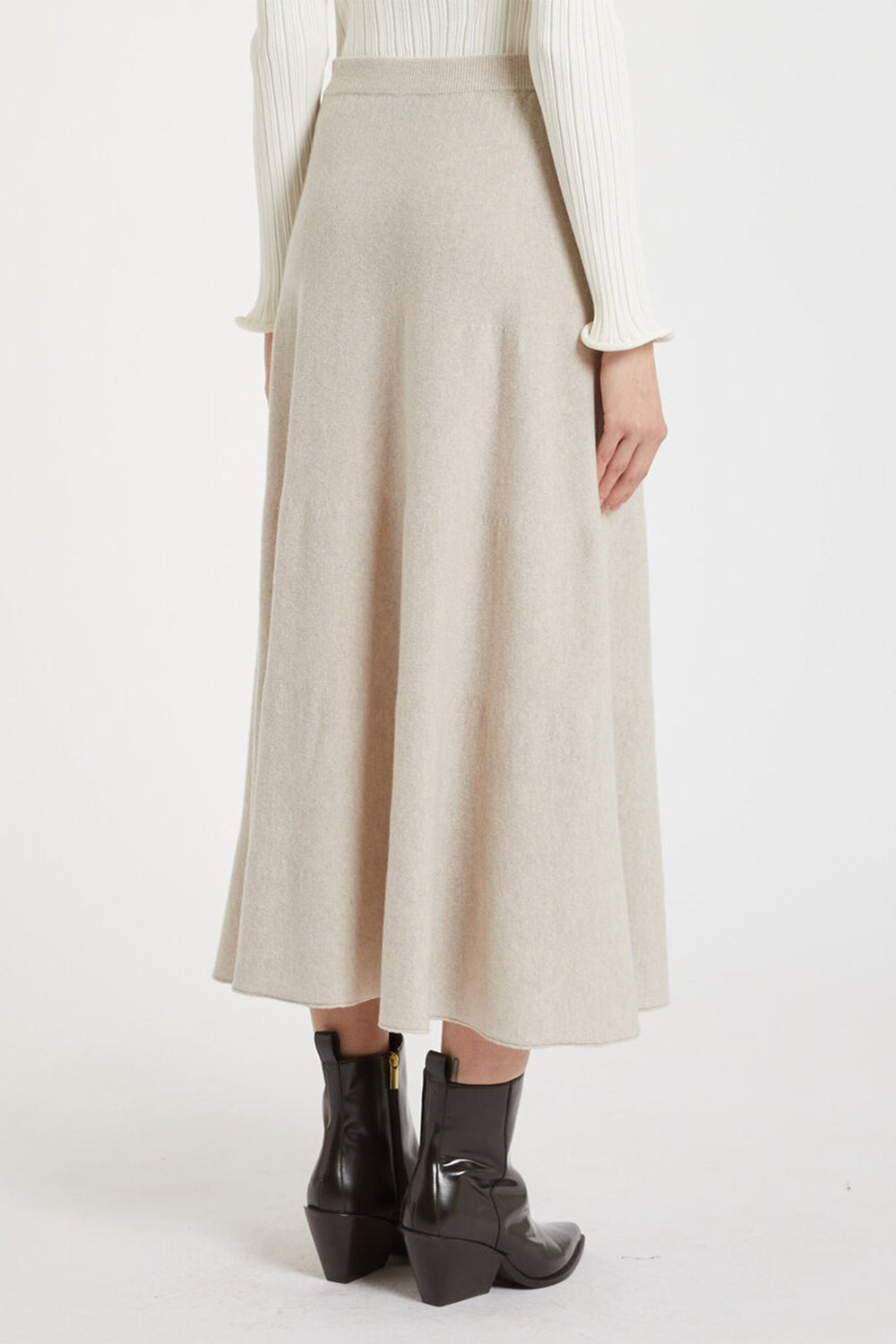 Person wearing a beige skirt and black boots on a white background