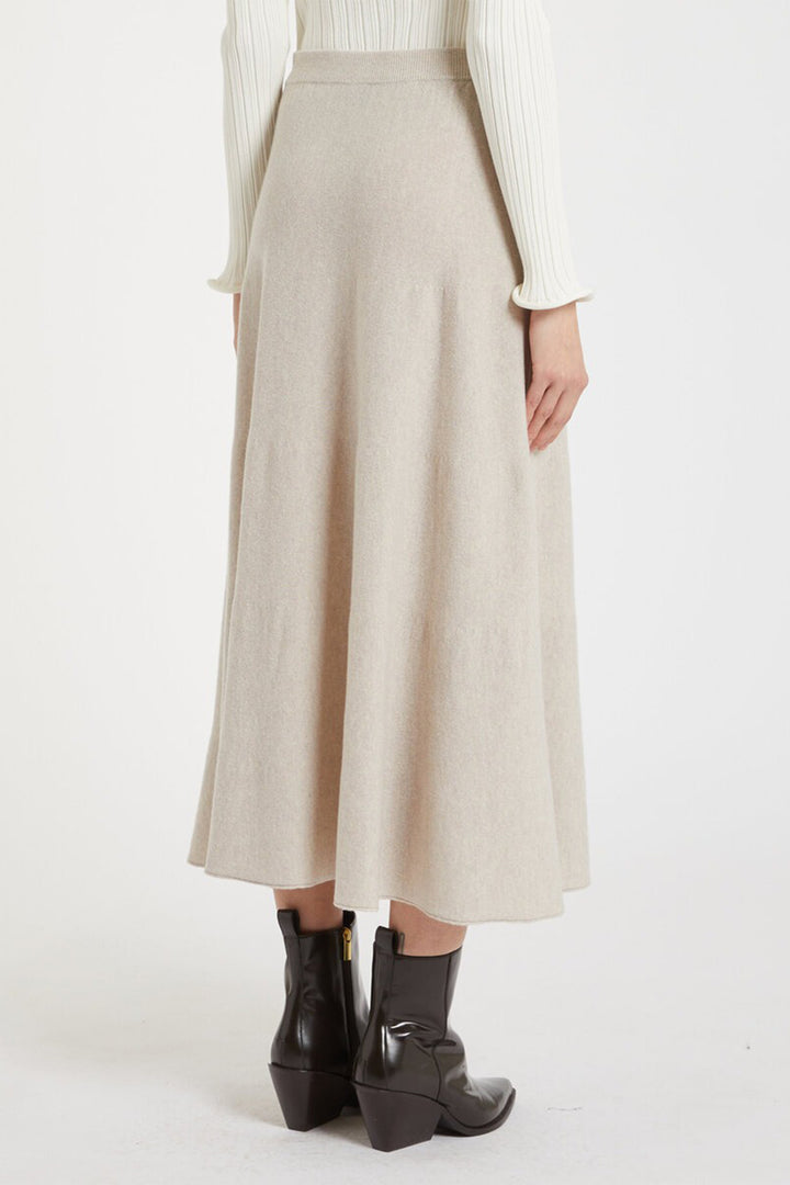 Person wearing a beige skirt and black boots on a white background