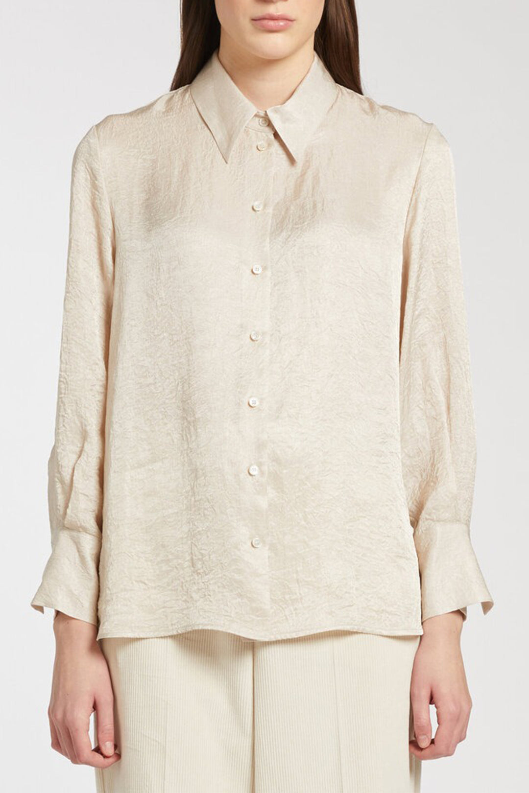 Woman wearing a beige button-up shirt and pants on a white background