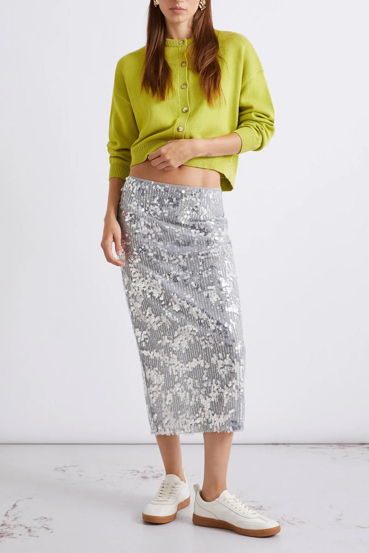 Person wearing a green cropped jacket and silver sequin skirt on a white background