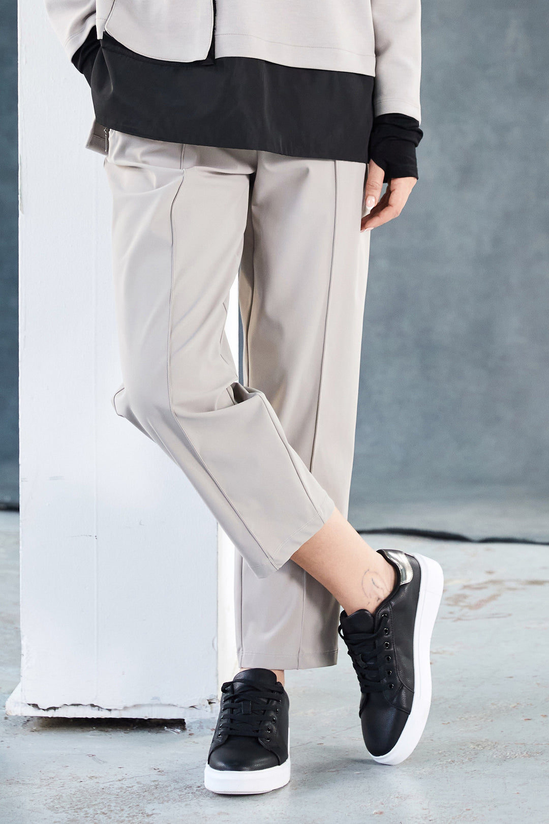 Person wearing light taupe pants and black sneakers against a neutral background