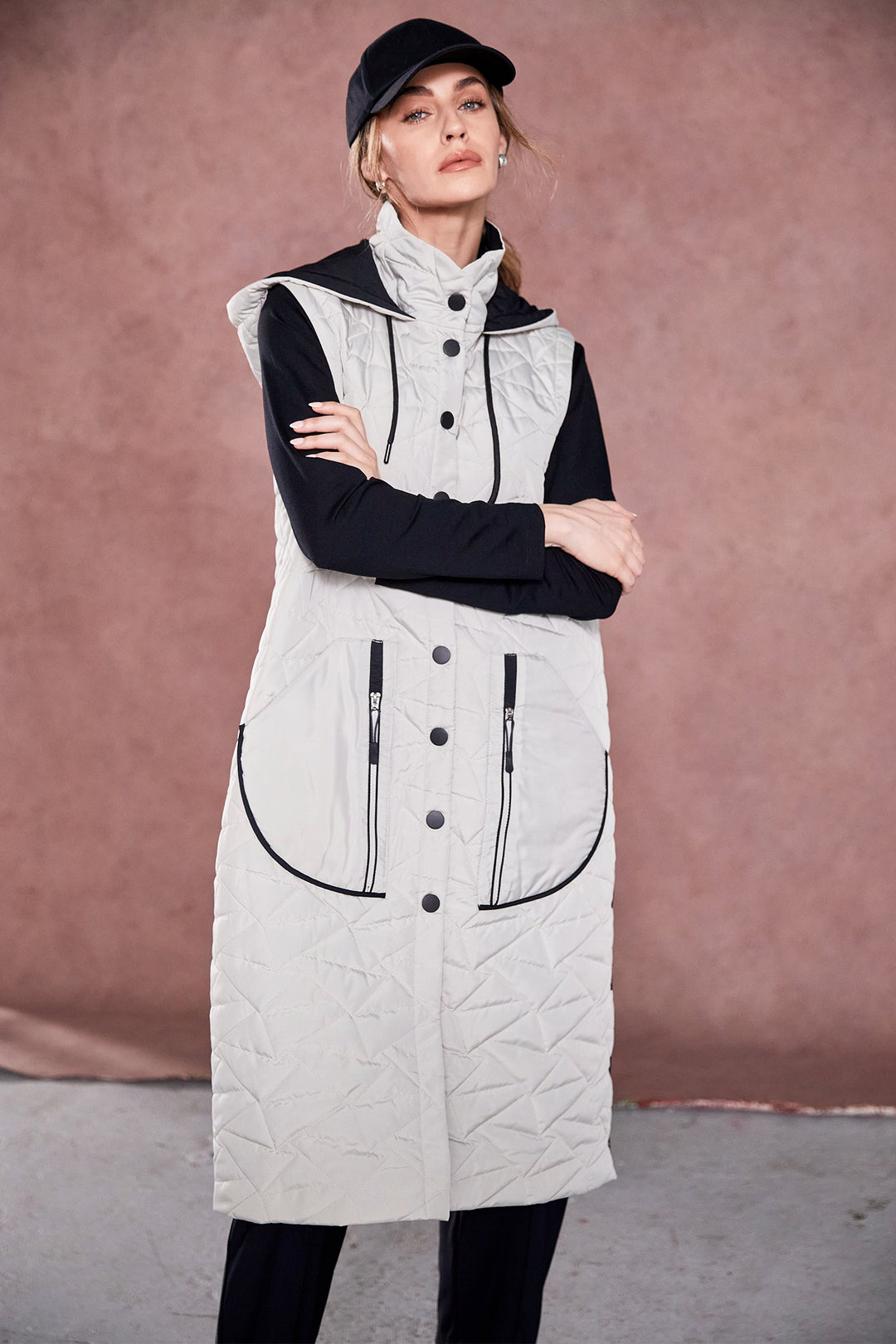 Woman wearing a long taupe quilted vest with black buttons and zippers against a brown background
