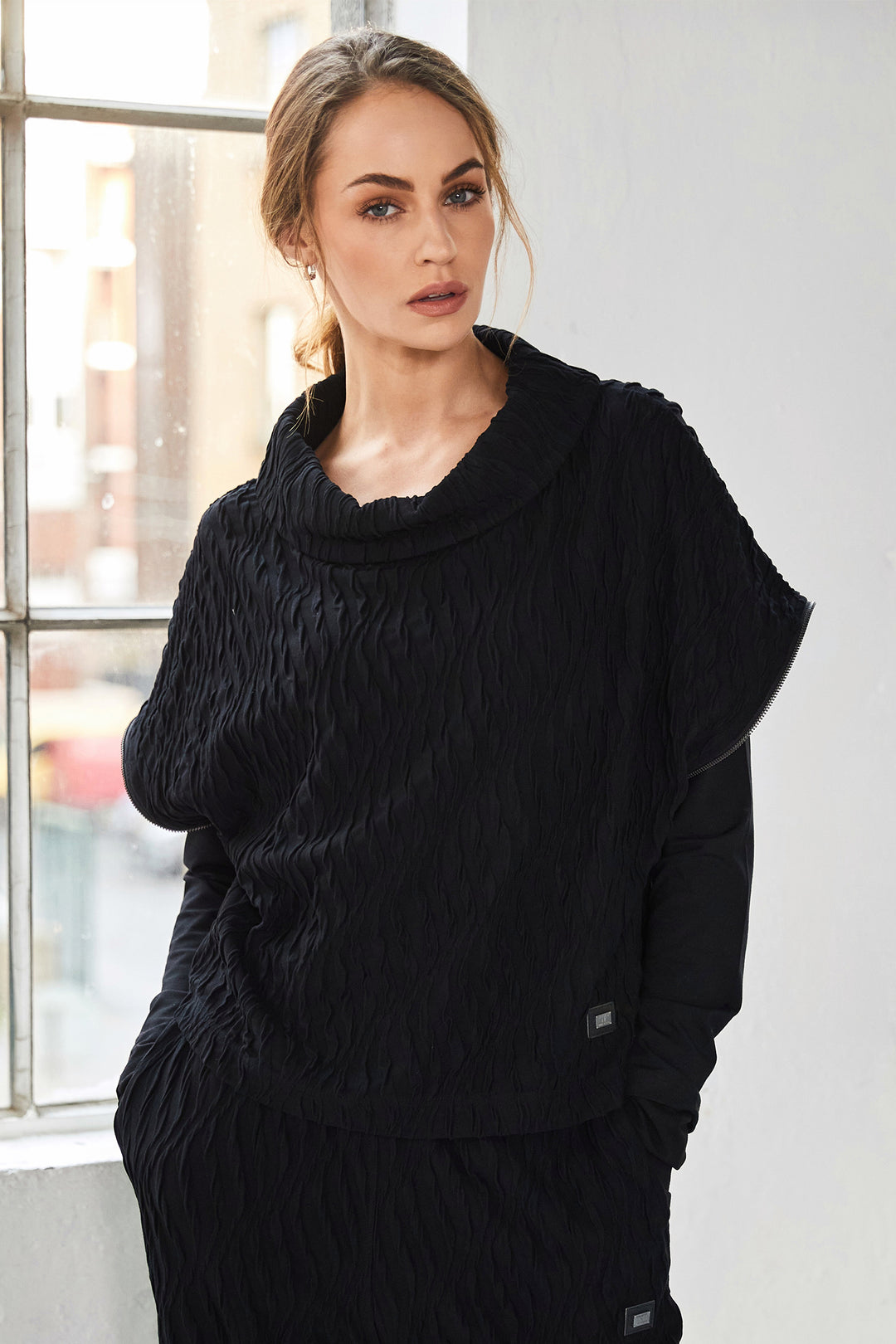 Woman wearing a black cable knit sweater in a room with a window.