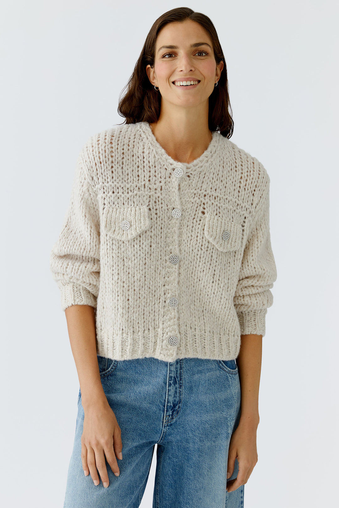 Woman wearing a beige knitted cardigan and blue jeans against a light background