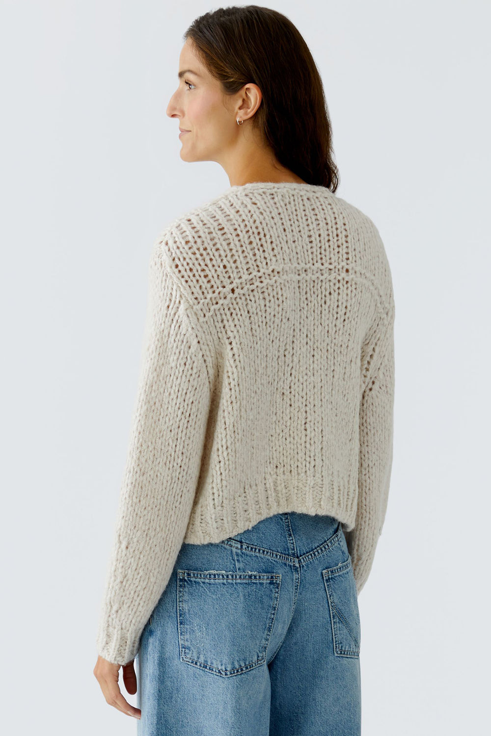 Woman wearing a beige knitted sweater and blue jeans on a light gray background