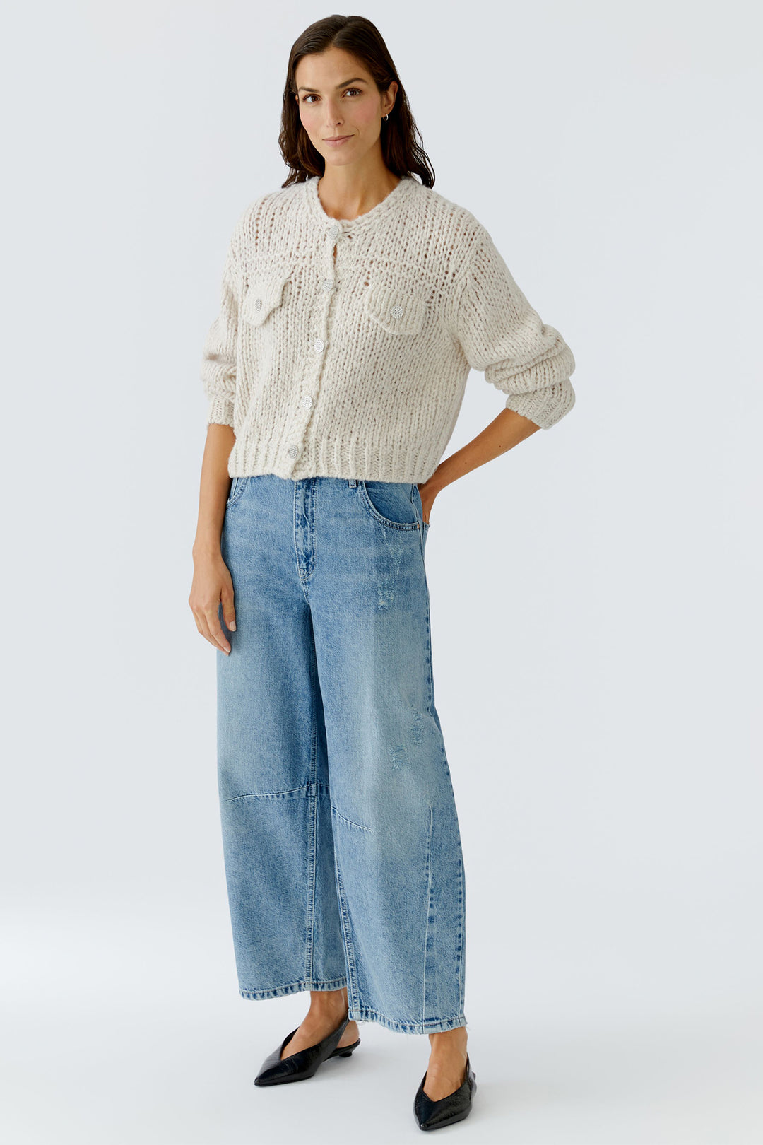 Woman wearing a cream knitted cardigan and blue jeans on a white background